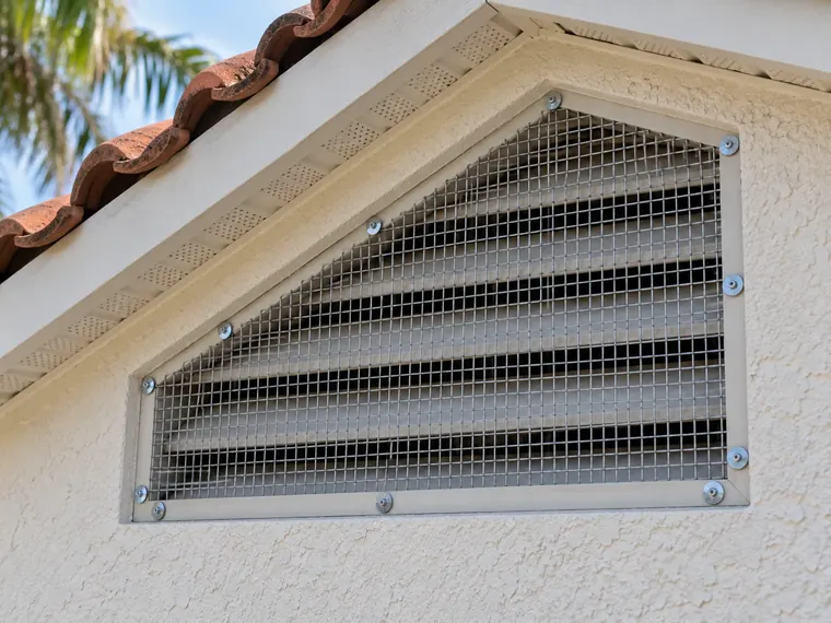 Gable vent on a stucco wall covered with galvanized hardware cloth fastened with screws and washers